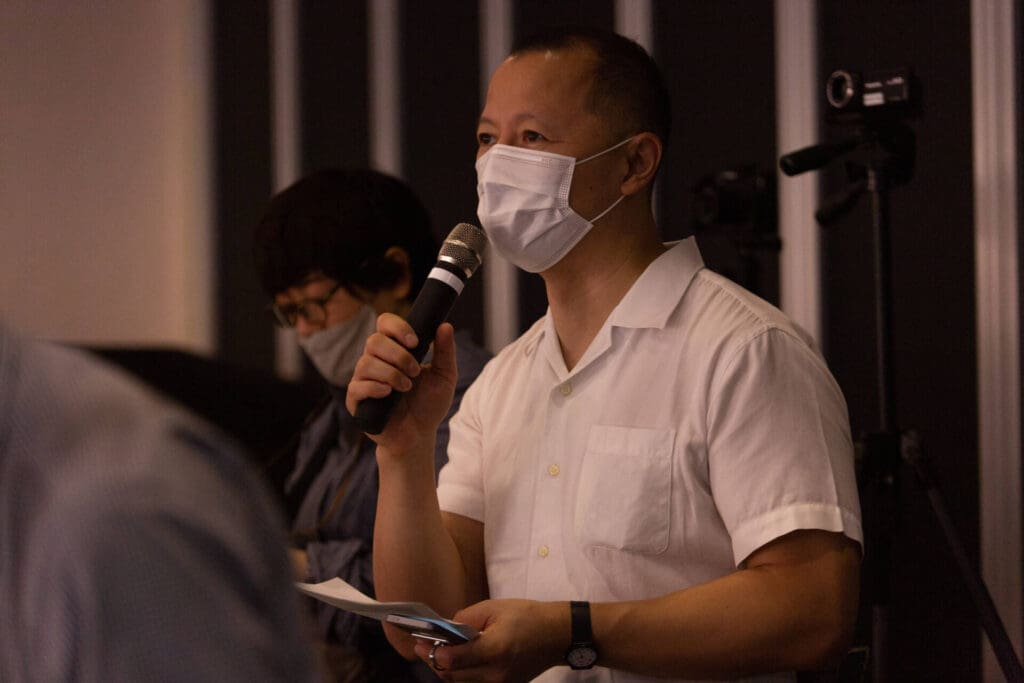 A man in a white shirt and face mask talking to others in a mic - Tokyo Portrait Photographer, Photographer in Tokyo